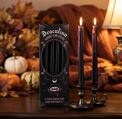 Een sfeervolle close-up foto van twee brandende Halloween kaarsen in een donkere, mysterieuze setting. De kaarsen hebben een griezelig effect waarbij roze was als tranen langs het zwarte kaarsvet naar beneden druipt.