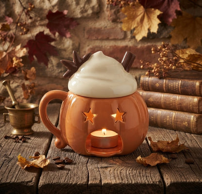 Een oranje pompoen waxbrander met een vrolijk design en een sfeervol brandend theelichtje erin. De achtergrond toont een warme herfstsfeer met een stenen muur, herfstbladeren, koffiebonen en vintage boeken.