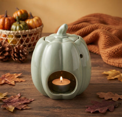 Saliegroene keramische pompoen waxmeltbrander met brandend waxinelichtje en los deksel. Gedecoreerd met herfstbladeren en bessen op een houten achtergrond.