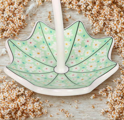 Close-up van een wit en groen sieradenbakje in parapluvorm, versierd met kleine witte bloemetjes en gekleurde regendruppels, perfect voor het opbergen van ringen en oorbellen