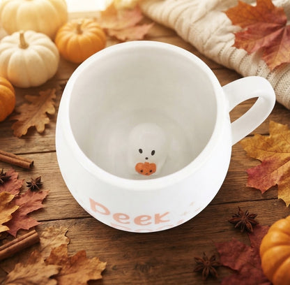 Van bovenaf bekeken herfstmok met een klein, wit spookje dat een pompoen vasthoudt op de bodem van de mok.