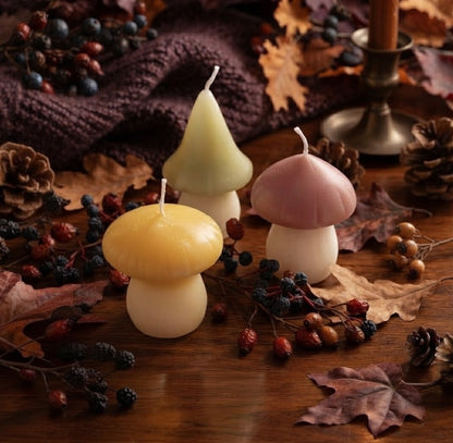 Drie kleurrijke paddenstoelenkaarsen speels opgesteld op een houten tafel, gedecoreerd met herfstbladeren, dennenappels en wilde bessen in een gezellige herfstsfeer.