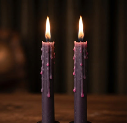Close-up productfoto van twee brandende zwarte Halloween dinerkaarsen die tijdens het branden unieke roze wasdruppels afscheiden. Deze griezelige stafkaarsen met griezelige wasdrip zorgen voor een angstaanjagend mooie sfeer en zijn de ideale griezeldecoratie voor je griezelige Halloween interieur en themfeesten.