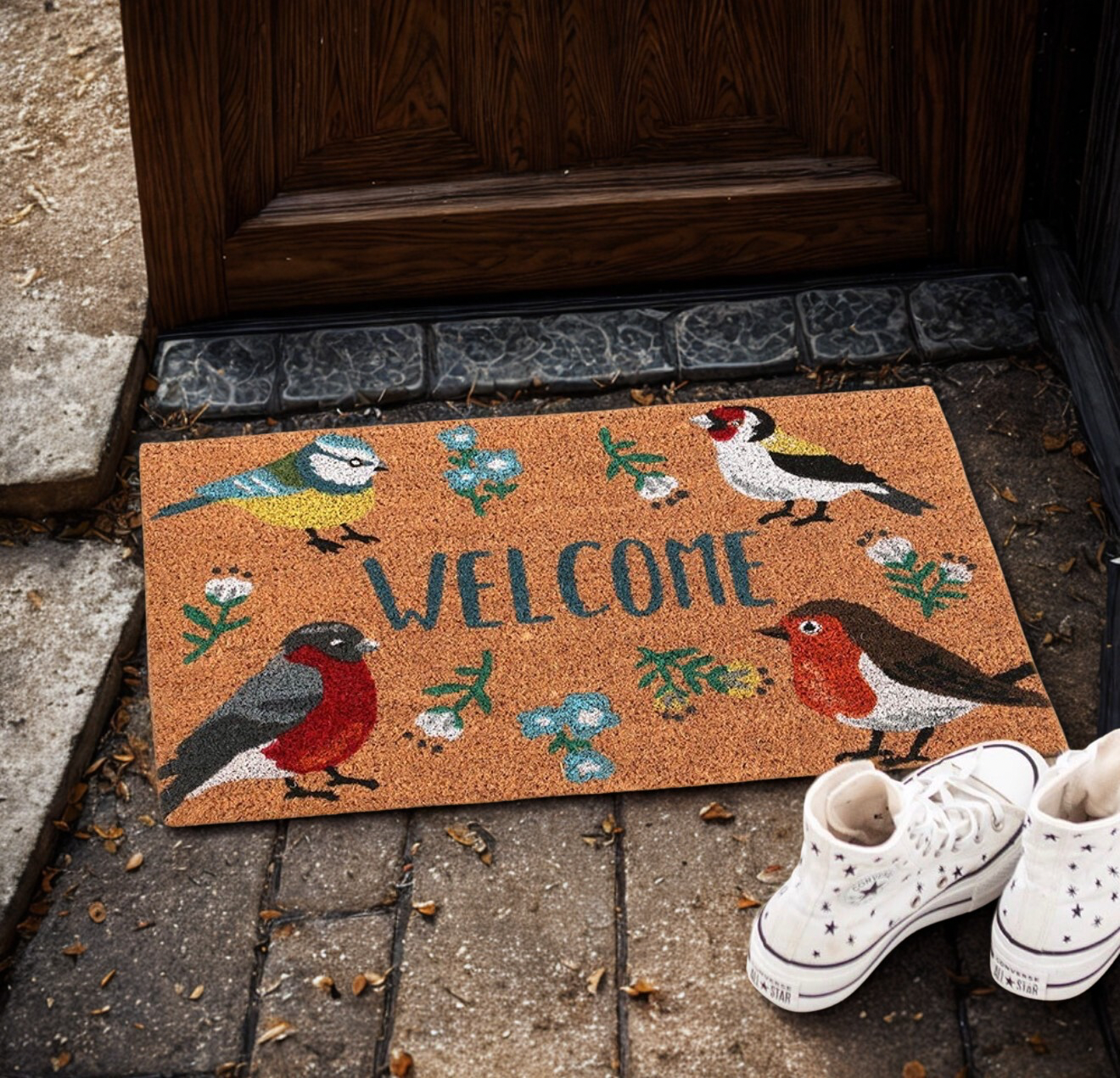Sfeervolle kokos deurmat met vrolijke tuinvogels en 'Welcome' tekst bij een voordeur.
